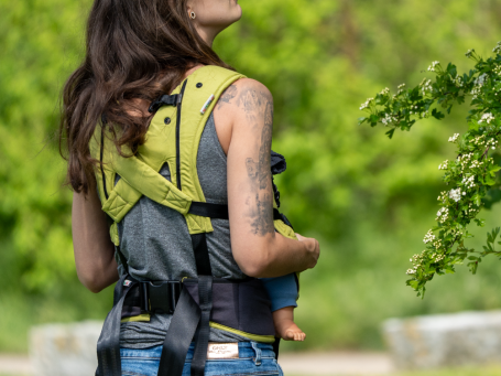 besondere Gurtführung Tragehilfe Frau mit Tätowierung trägt ein Baby in einer Tragehilfe, man sieht den Rücken und die besondere Gurtführung der Trage